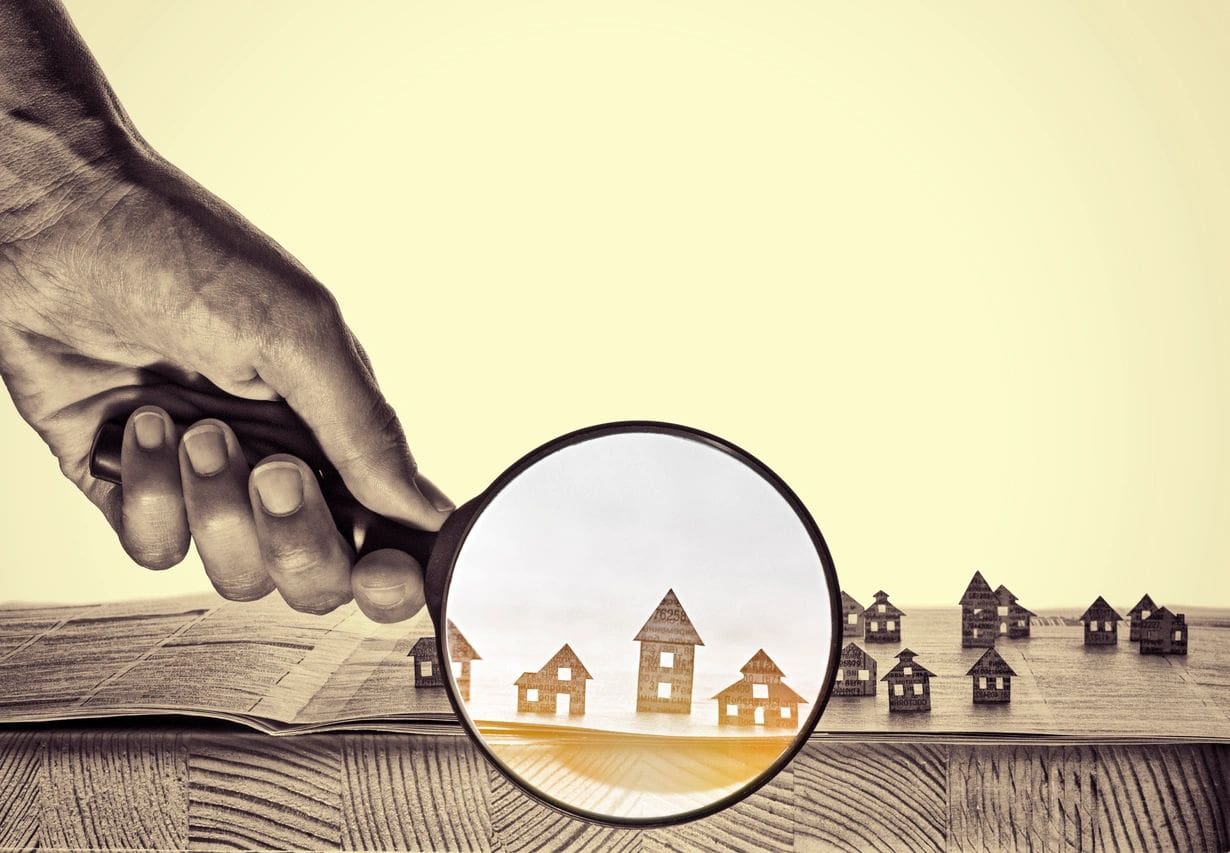A hand holding a magnifying glass over a group of houses.